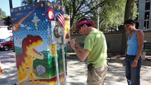 From left, local artist Kurt Piller paints an electrical box on the corner of Aurora and Buffalo Streets while Janaki Parthasarathy, of Ithaca, looks on. Piller’s box was a part of the “21 Boxes” project.