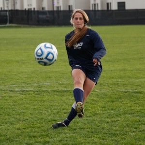 Senior forward Rachael Palladino stands in front of a net filled with 59 soccer balls on Carp Wood Field. with 59 career goals, she is closing in on the Bombers record of 61 set by Chelsey Feldman ’09.