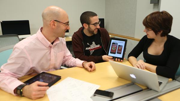 From left, Adam Peruta, assistant professor in the department of strategic communication, points to a Chipotle app as junior Noah Delin looks on. 