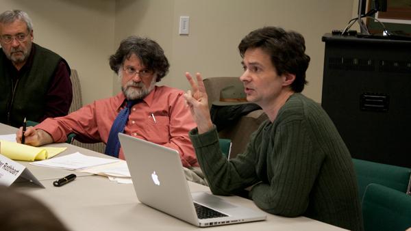 From left, Peter Rothbart, professor of music theory, history and composition, listen as Steven Skopik, chair of media, arts sciences and studies and representative of the Faculty Handbook Amendment Committee, addresses the Faculty Council Tuesday in the VIP Room in the A&E Center. 