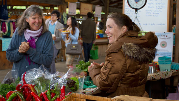 From left, a patron walks by Courtney Sullivan’s farm booth  Sunday at the Ithaca Farmer’s Market at Steamboat Landing.