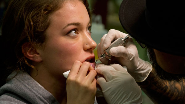 Junior Hannah Wright looks up as Medussas Tattoo Studio artist, Cesar Enciso tattoos the letters ICXC onto her bottom lip.