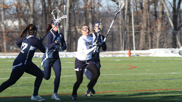 Senior defender Katie Long carries the ball up the field while three SUNY Geneseo players chase her in the women’s lacrosse game March 6 at Higgins Stadium. The Knights defeated the Bombers 10–7.
