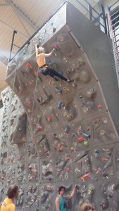 A staffer at the Ithaca College climbing wall pulls herself up over the incline to finish a route.