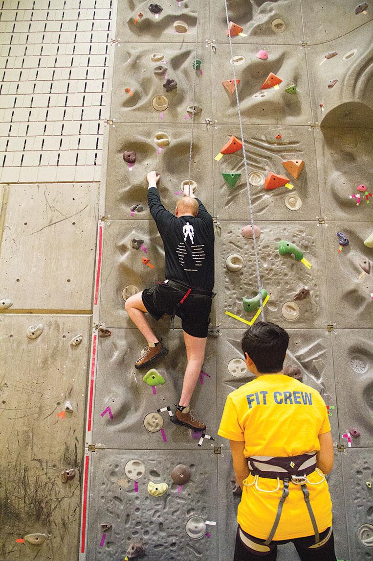 Corey Hess/ The Ithacan Tim climbs the rock wall in the Fitness Center with the help of a student staffer April 9.