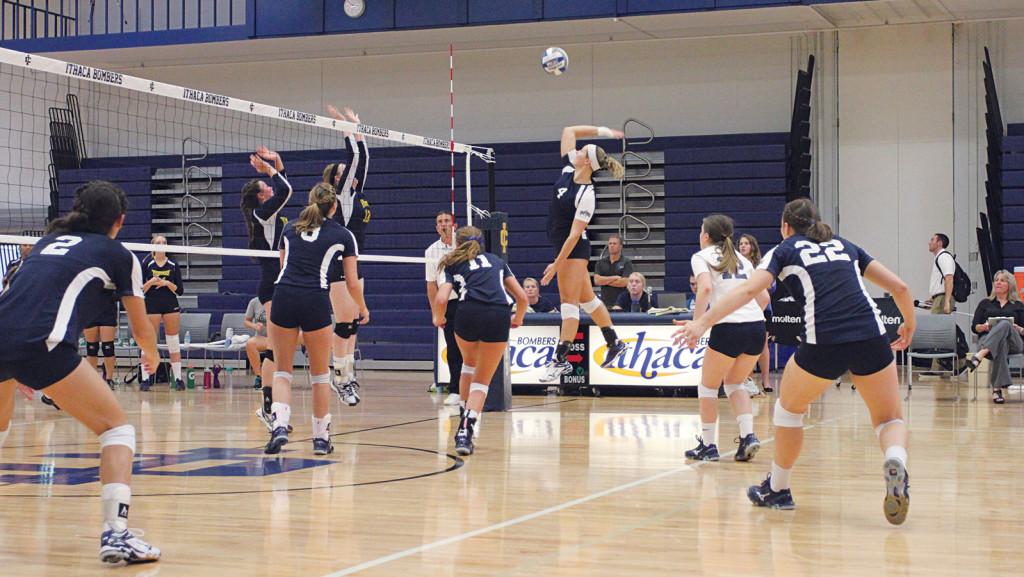 Right, sophomore Caroline Gerulskis spikes the ball as her teammates look on intensely during a match Sept. 5, 2014, at Ben Light Gymnasium.