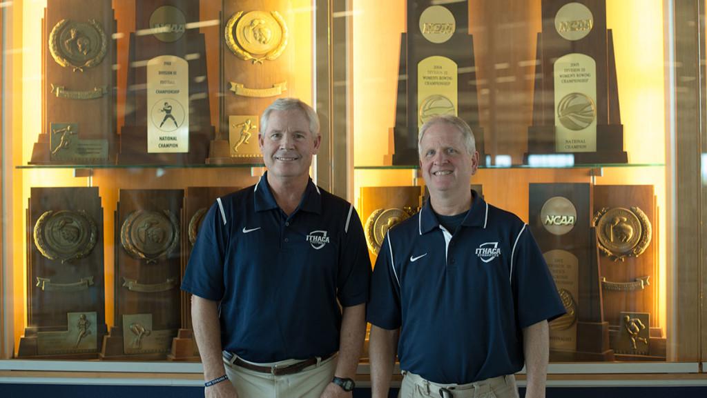 Head coaches Mike Welch, football, and Rick Suddaby, gymnastics, stand side-by-side in front of the trophy case inside the Athletics and Events Center. They are both going to be inducted into the Athletic Hall of Fame during the 2015 ceremony on Sept. 25 along with six other alumni and two teams.