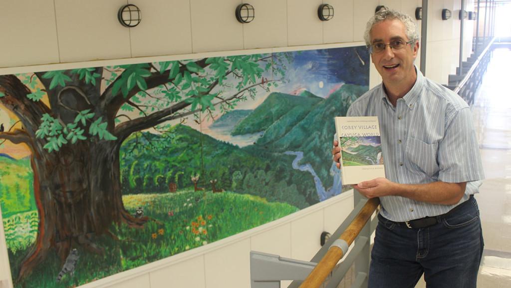 Professor Jack Rossen poses in front of the mural in Williams Hall that inspired the cover for his new book.