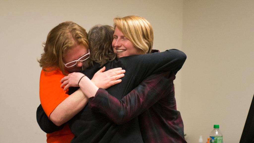 Megan Graham, assistant professor, left, and Rachel Gunderson, former instructor, hug Shoshe Cole, former assistant professor, after signing the final contingent faculty contract March 26. 
