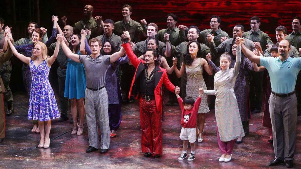 Former student Emily Bautista, to the left in a solid blue dress, and the current cast of Miss Saigon during opening night curtain call. The play takes place during the Vietnam War era.