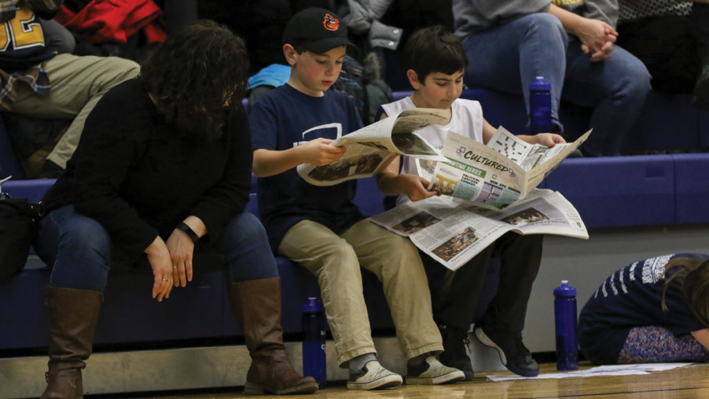 From left, 9-year-old Kai Patrone and 10-year-old Elliot Cullenen read The  Ithacan during men’s basketball’s 85–63 win against Bard College in Ben Light  Gymnasium on Feb. 16. Patrone said it is his dream to have a photo in The Ithacan. 
