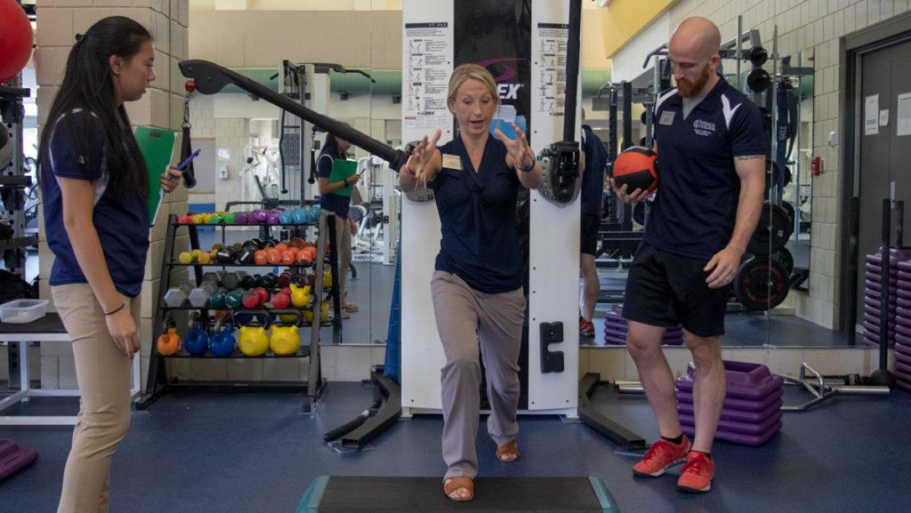 Jill Mayer, a clinical assistant professor in the Department of Physical Therapy, demonstrates an exercise to senior Tayler Tai (left) and graduate student Matthew Limoges (right). Mayer founded a program pairing local cancer survivors with students and clinicians at the college to study and develop personalized fitness plans. 
