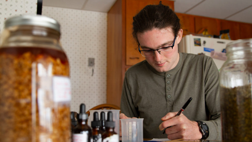 Senior Mike Hanlon calculates the amount of alcohol and water to mix with damiana leaf, a plant that can be used as an aphrodisiac, to help stomach issues and to help diminish symptoms of premenstrual syndrome. Hanlon has taken classes at Ithaca College and apprenticed with a local herbalist to learn the craft.