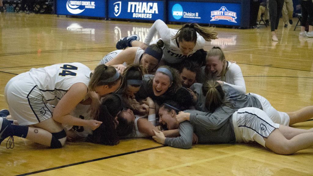 Members of the Ithaca College womens basketball team pile on top of senior Annie Giannone at the end of overtime after she sank a layup to secure the Bombers victory over RIT and the teams first-ever Liberty League Championship.