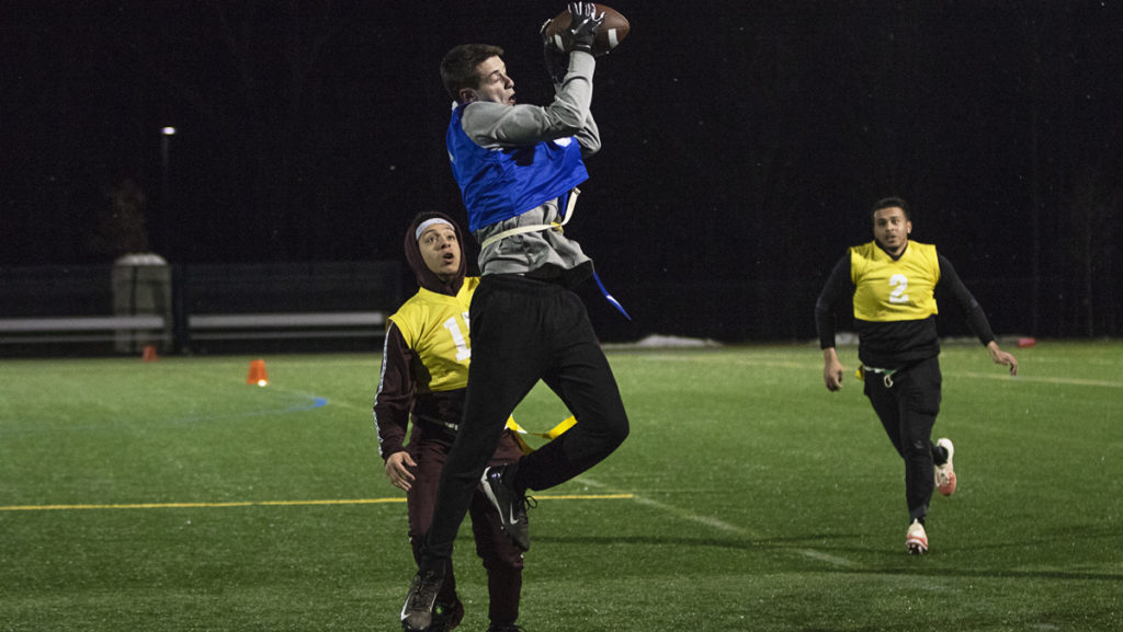 Sophomore Gabe Gomez and freshman Steven Bailey in yellow look on as freshman Ben Cohen in blue makes a catch for his team, the Washed Up Pros. The intramural flag football league plays Sunday Evenings.