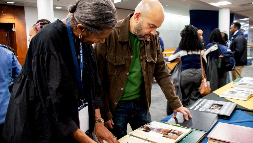 From left, Traci Hughes and Carlos Velez, class of '85, flip through old photo albums Oct. 12 at the Higher Education Opportunity Program's 50th Anniversary celebration in the James J. Whalen Center for Music. 