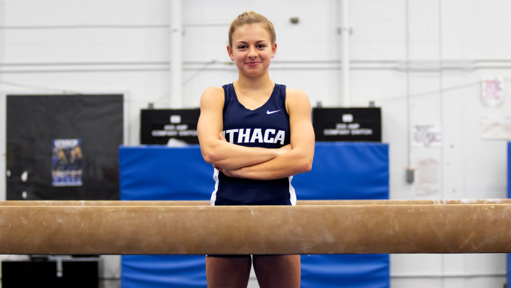 Sophomore Katelyn Sarkovics poses next to the balance beam on which she used to compete, in her newly-earned cross-country uniform. The athlete transitioned from gymnastics to running in Fall 2019.