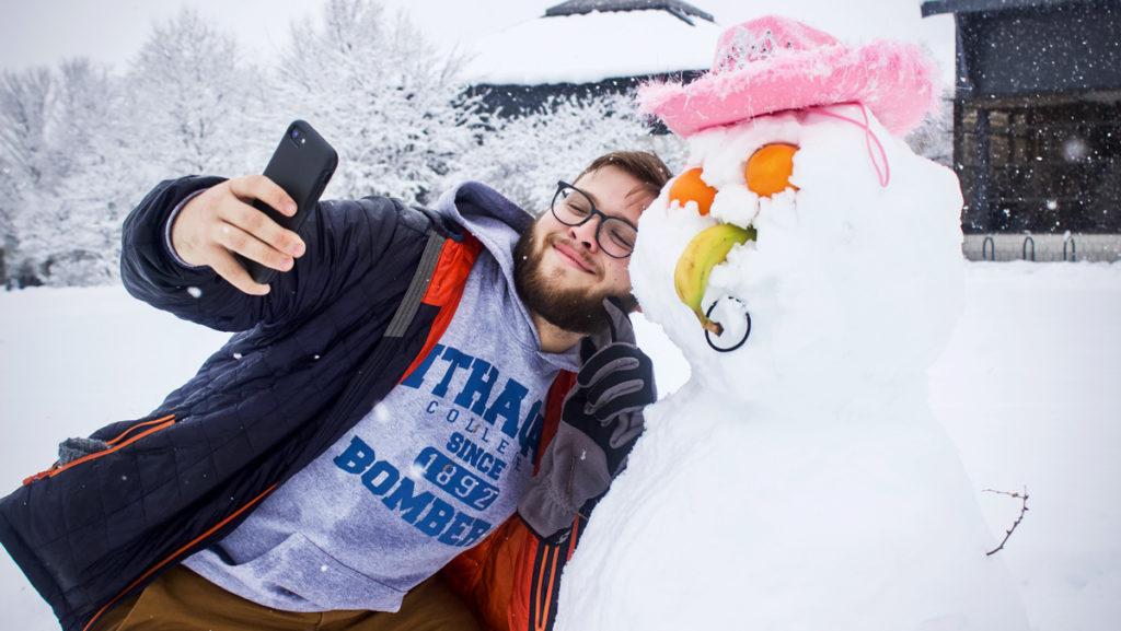 Freshman Zack Lemberg takes a photo with a snowman he built Dec. 2. It is named Diane. Ithaca College canceled classes Dec. 2 due to inclement weather. Approximately 6­–12 inches of snow fell in the Ithaca area from Dec. 1 to 3.  				             
