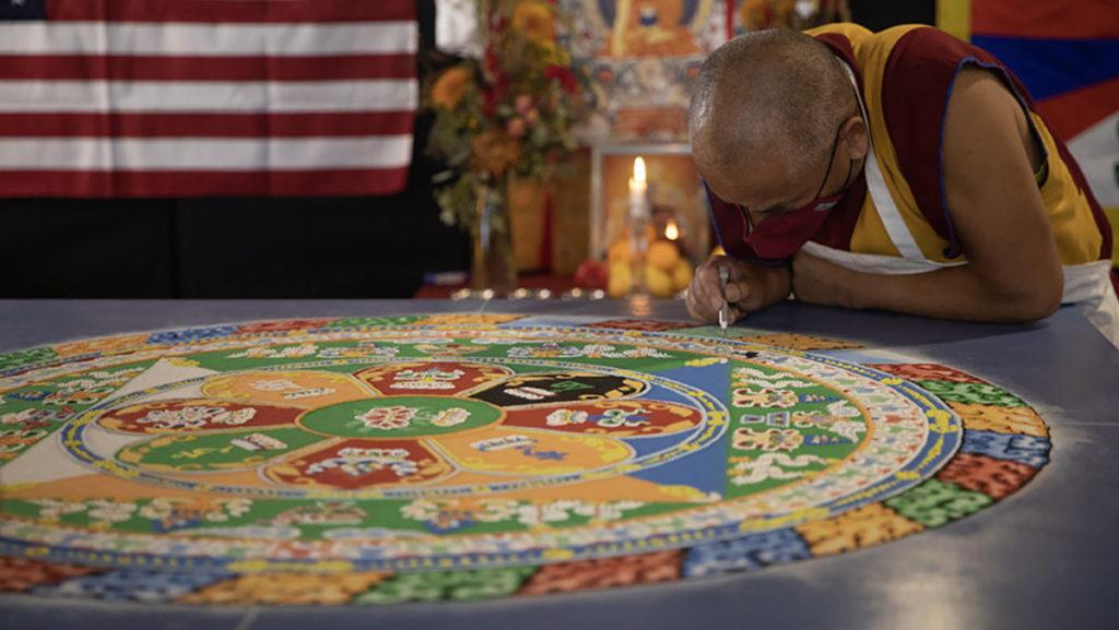 Venerable Namgyal, a visiting buddhist monk, works on a mandala in the lobby of the Campus Center. The intricately designed mandala was created with colored sand and represents Chenrezig, which is recognized by Tibetan Buddhists as the bodhisattva of compassion. 