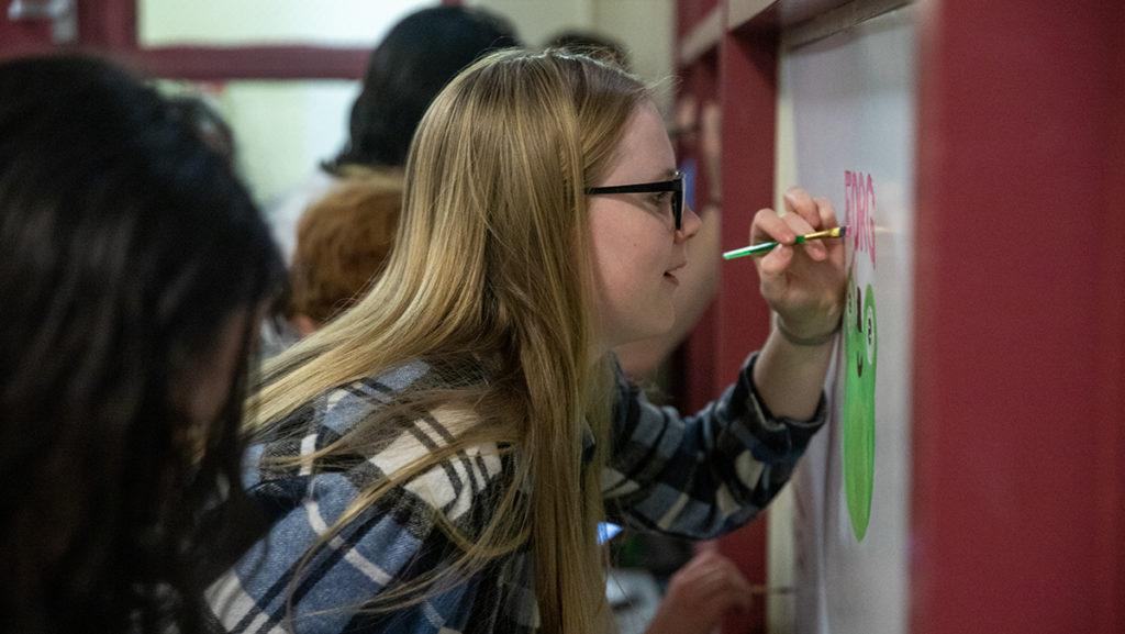 Sophomore resident assistant Taylor Hagquist paints on one of the boards in the hallway outside the Landon Hall lounge Feb. 26. The event was hosted by senior RA Alexis Danielson, and free snacks were provided to residents who attended.
