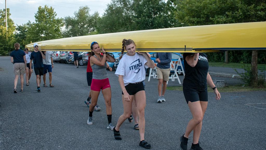 From left, Devi de Olivera 23 and Allison Arndt 23 carry a boat by the Cayuga Inlet. Arndt, a decorated graduate of the program, was recently named a finalist for the CRCA Athlete of the Year award.