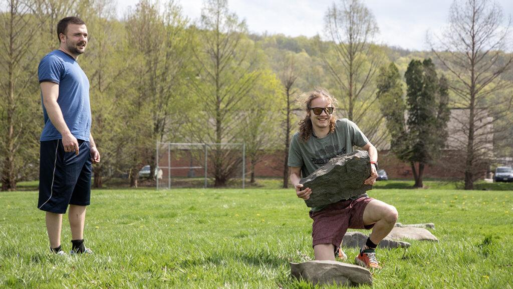 From left, senior Leo Baumbach looks on as sophomore Conrad West advances through the stone ladder during the “Stoned by the Creek” strongman competition on April 22.