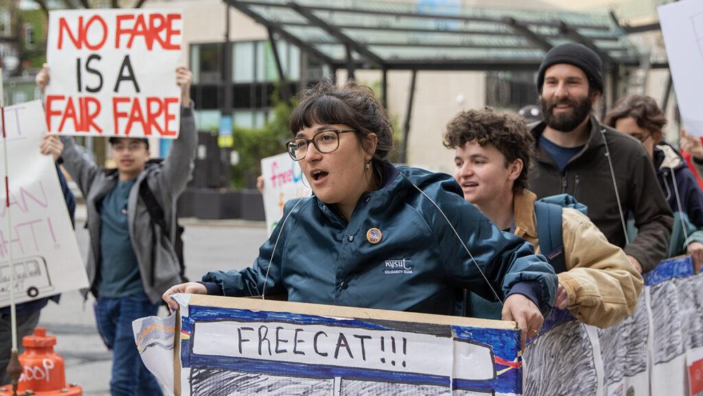 From left, Earl de los Santos holds up a sign while Aurora Rojer, Katie Sims and Adam Hart hold up a cardboard version of a FreeCAT May 2 on the Commons.
