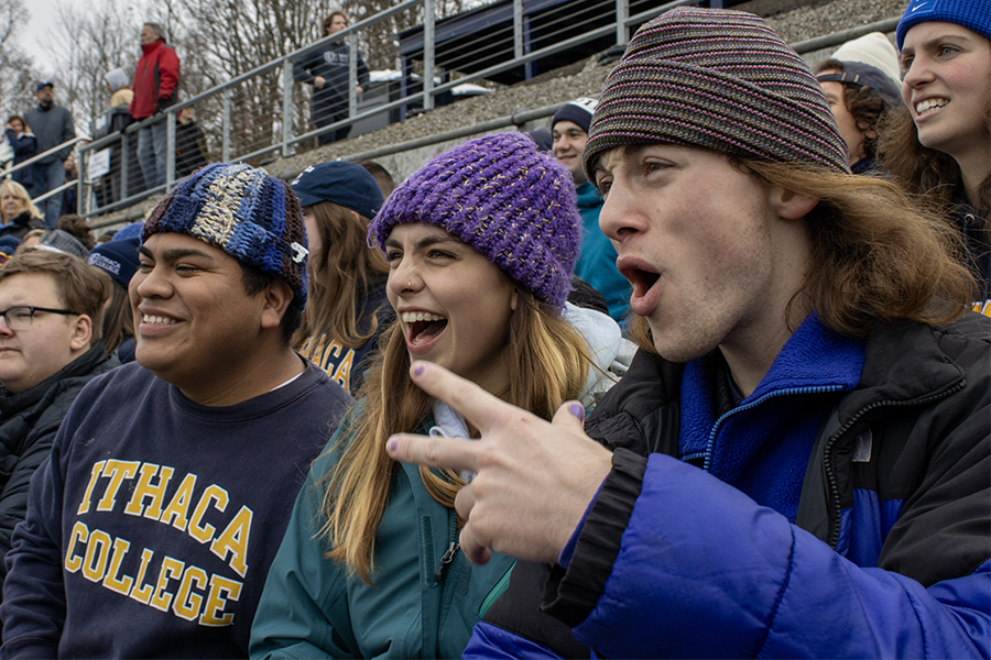Left to right, seniors Eddie Santos, Delia Ablard and Arthur Robbins-Geller cheer for the Ithaca Bombers as they take the field to start the 2023 Cortaca Jug. 