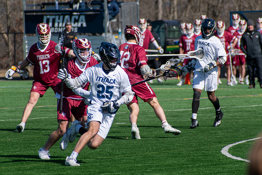 Junior attackman Jack Pastore carries the ball in his stick with several defenders trailing behind. The Bombers secured a 12–10 victory in the late stages of the game against the St. John Fisher University Cardinals.