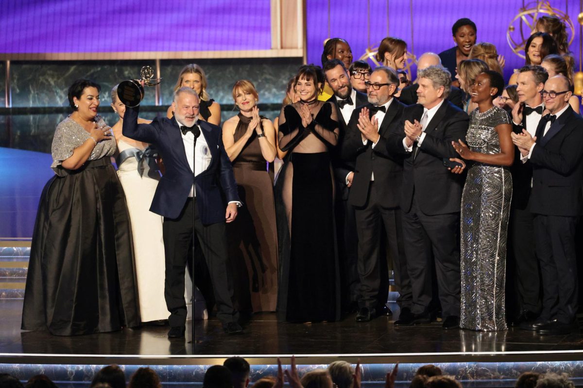 R. Scott Gemmill stands holding the trophy for outstanding drama series with cast and crew surrounding him clapping and cheering on stage.