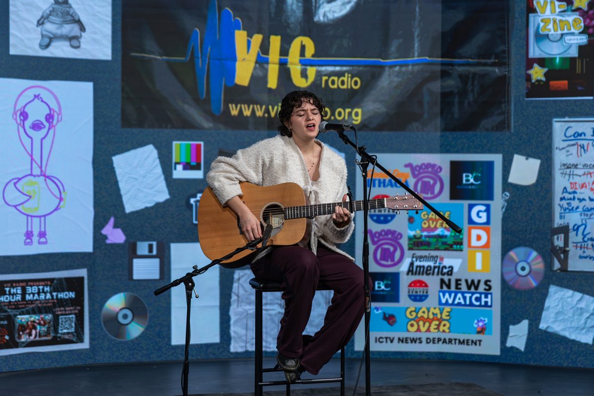 Senior Isabella Joyner strums and sings one of her original songs in ICTV's Studio A. The background, created by station manager junior Romeo Maslin, features posters and memorabilia from both ICTV and VIC events. 