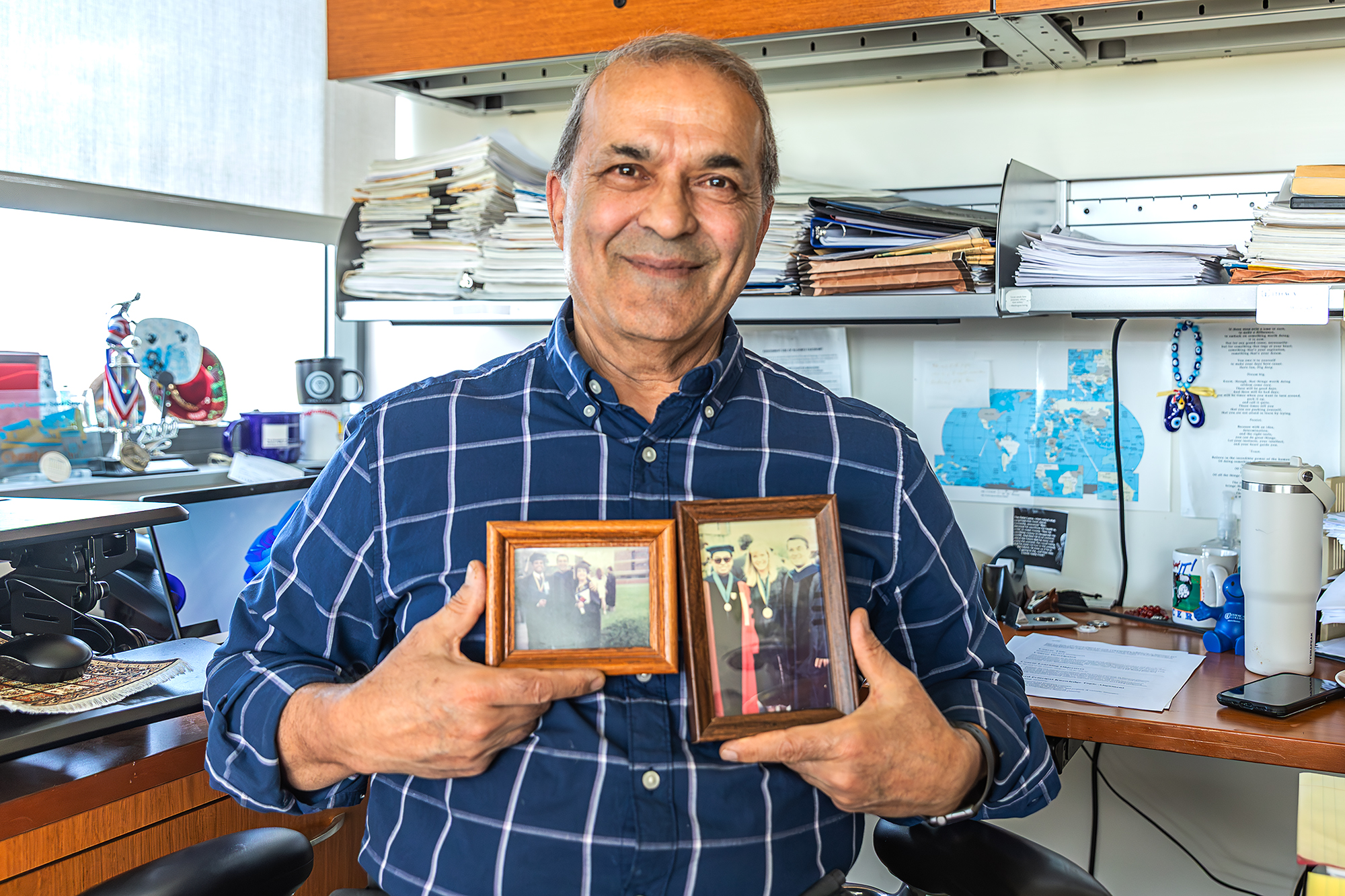 Hormoz Movassaghi, professor and chair of the Department of Finance and International Business at Ithaca College, holds photos of himself posing with graduating students and a colleague after commencement in the early 1990’s.