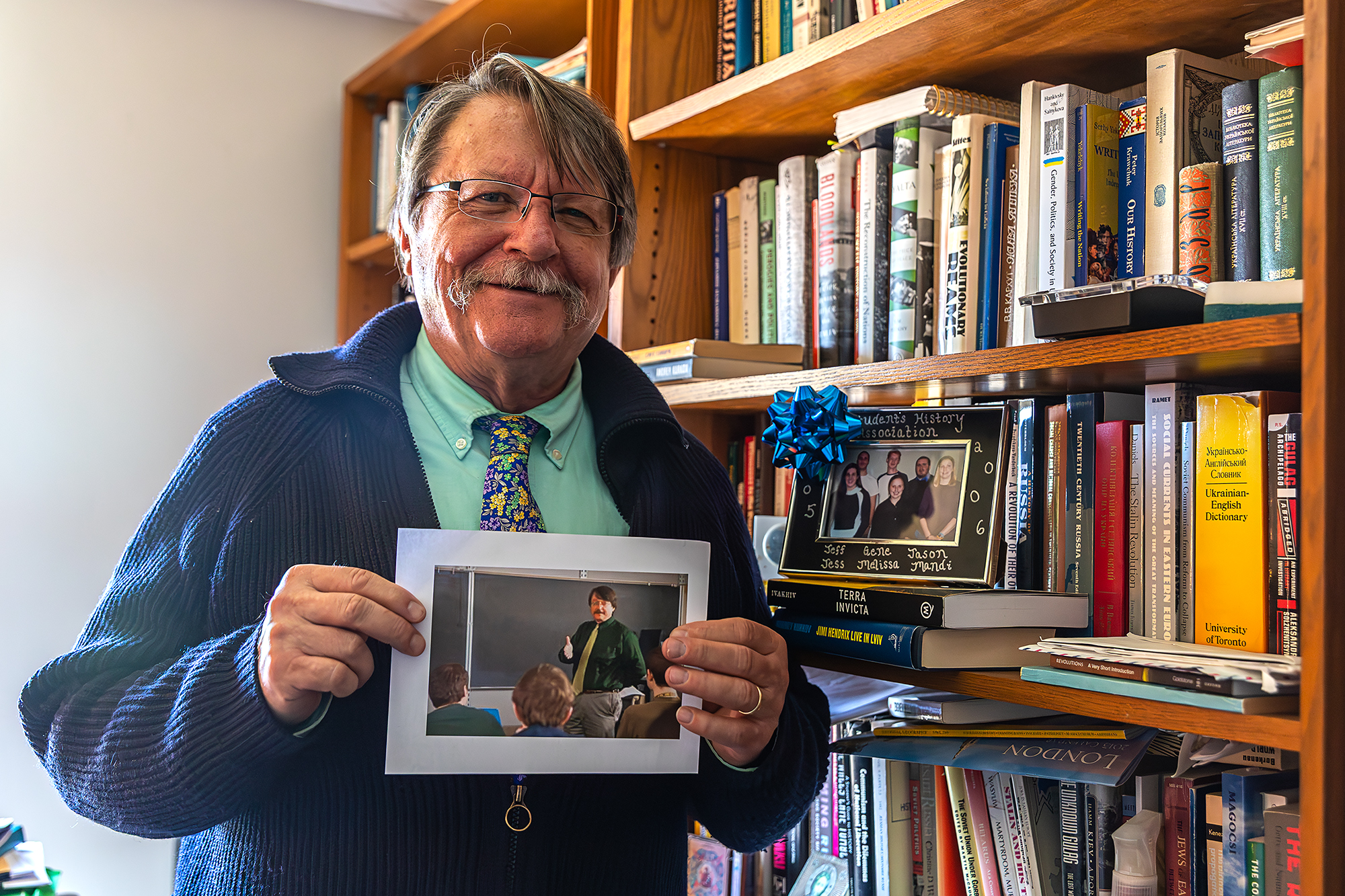 Zenon Wasyliw, professor in the Department of History at Ithaca College, holds a photo of himself teaching in the early 2000’s next to a framed photo of the 2005-2006 Students History Association members.